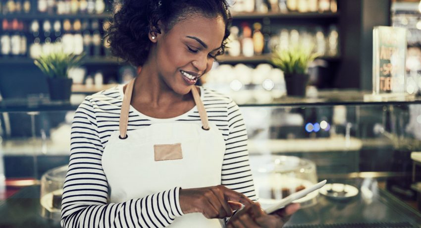 Young African entrepeneur standing in her cafe using a tablet