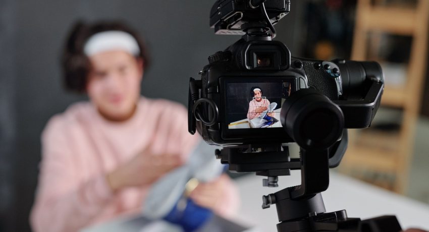 Young vlogger in casualwear showing sneakers on display of digital video camera